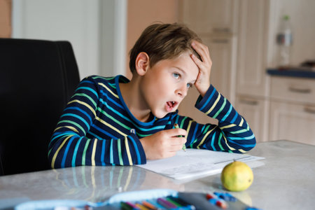 Hard-working happy school kid boy making homework during quarantine time from corona pandemic...