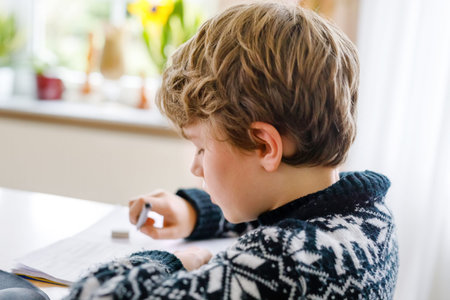 Hard-working happy school kid boy making homework during quarantine time from corona pandemic...