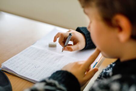 Hard-working happy school kid boy making homework during quarantine time from corona pandemic disease. Healthy child writing with pen, staying at home. Homeschooling conceptの写真素材