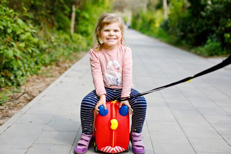 little toddler girl walking in park pandemic coronavirus disease. Cute adorable child playing with toy car suitcase on wheelsの写真素材