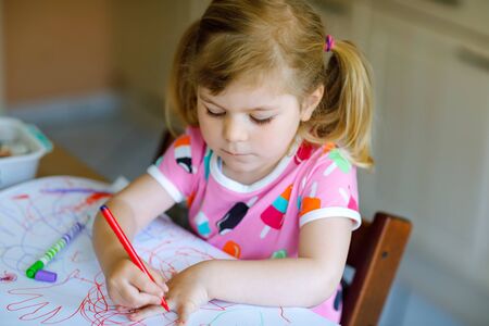 little toddler girl painting with different colorful pens and felt pencils during pandemic coronavirus quarantine disease. Child alone at home, closed nurseryの写真素材