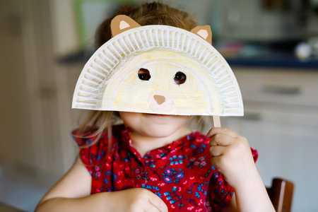 little toddler girl painting with finger colors making animal bear mask during pandemic coronavirus...