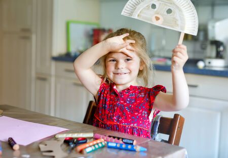 little toddler girl painting with finger colors making animal bear mask during pandemic coronavirus quarantine disease. Happy creative child, homeschooling with parentsの写真素材