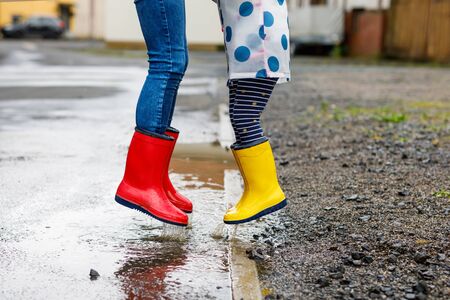 Close-up of two children, toddler girl and kid boy wearing red and yellow rain boots, walking during sleet. Happy siblings, brother and sister jumping into puddle. Having fun outdoors, active family.の写真素材