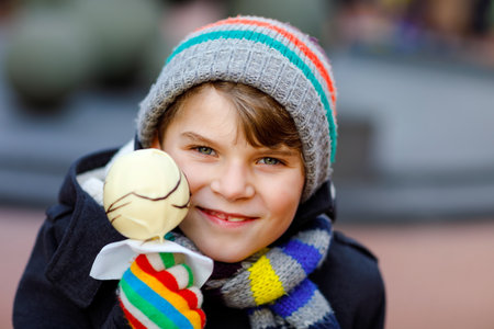 Little cute kid boy eating white chocolate covered fruit apple on skewer on traditional German Christmas market. Happy child on traditional family market in Germany during snowy dayの写真素材