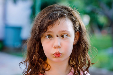 Portrait of little school girl with ladybug on face. Happy smiling excited child on warm summer...