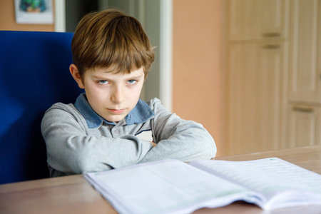 Upset school kid boy making homework during quarantine time from corona pandemic disease. Crying and...