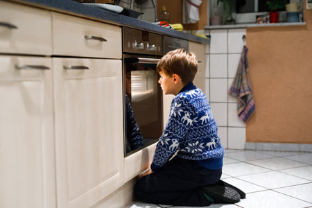 Cute funny blond kid boy baking muffins in domestic kitchen. Child having fun with helping, sitting...