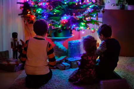Two little kid boys and adorable toddler sitting by Christmas tree with old vintage toys and balls with lots of present on Xmas eve. Family preaparation celebration of family feastの写真素材