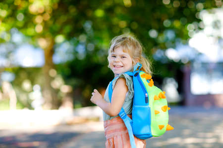 Cute little adorable toddler girl on her first day going to playschool. Healthy beautiful baby walking to nursery preschool and kindergarten. Happy child with backpack on the city street, outdoors.の写真素材