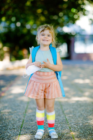 Little toddler girl on her first day on way to playschool with medical mask against corona covid...