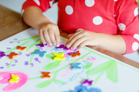 Little toddler girl playing with different colorful stickers and painting flowers. Concept of...
