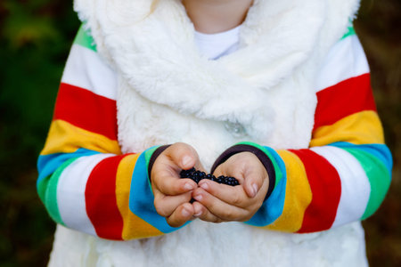 Cute little toddler girl making a walk through autumn forest. Happy healthy baby eating...