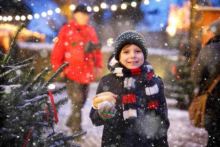 Little cute kid boy eating German sausage and drinking hot children punch on Christmas market. Happy child on traditional family market in Germany. Laughing boy in colorful winter clothesの写真素材
