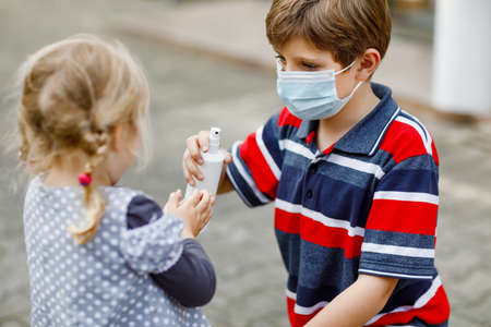 School kid boy helping little toddler sister cleaning hands with sanitizer spray. Brother and cute little girl learn hygiene rules. Family during coronavirus and flu lockdown. Covid virus protection.の写真素材