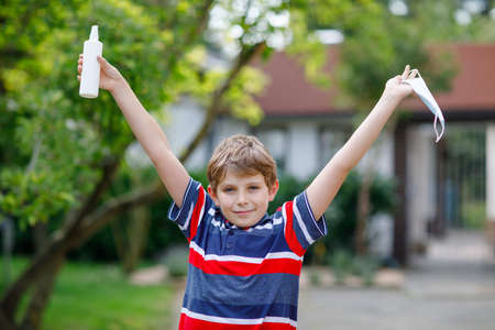 School kid boy with medical mask as protection against pandemic coronavirus quarantine disease. Child holding bottle with sanitizer for cleaning hands. protective equipment against covidの写真素材
