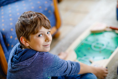 Happy kid boy playing table soccer with friends at home. Smiling child having fun with board...