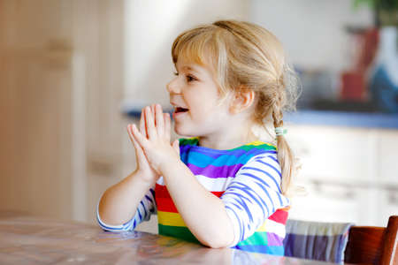 Cute toddler girl praying to God at home. Child using hands for pray and thank for food. Christian tradition.の写真素材