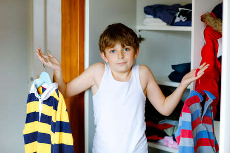School kid boy standing by wardrobe with clothes. Child making decision for school shirt to wear. Children get dressed in the morning for school.の写真素材