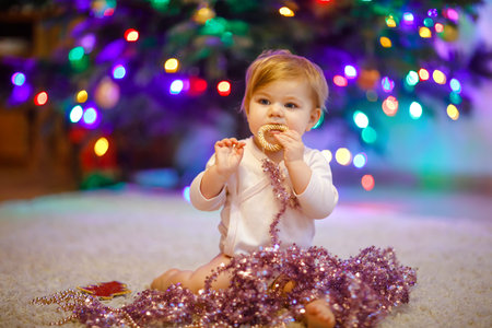 Adorable baby girl holding colorful lights garland in cute hands. Little child in festive clothes...