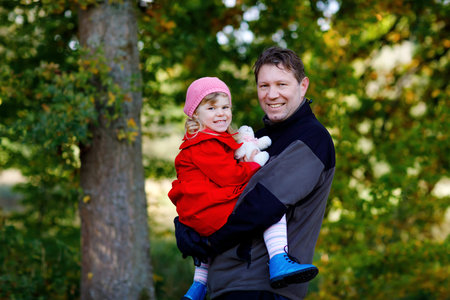 Happy young father having fun cute toddler daughter, family portrait together. Middle-aged Man with beautiful baby girl in autumn forest or park. Dad with little child outdoors, hugging. Love, bondingの写真素材