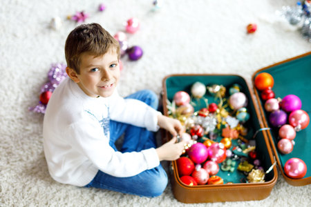 Beautiful kid boy and colorful vintage xmas toys and ball in old suitcase. Child decorating...