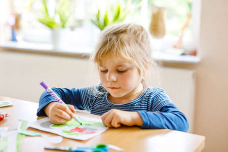 Little toddler girl painting animals and using scissors. Concept of activity of children during pandemic corona virus quarantine. Child learning colors with parents at homeの写真素材