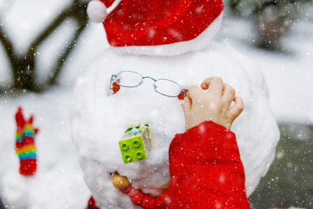 Little kid putting eye glasses on snowman. Close-up. child having fun with first snow in winter