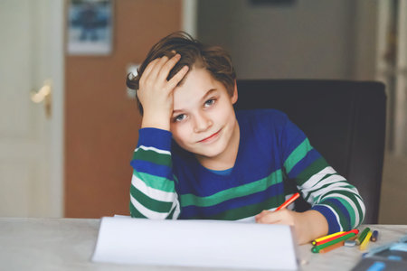 Portrait of cute happy school kid boy at home making homework. Little child writing with colorful...