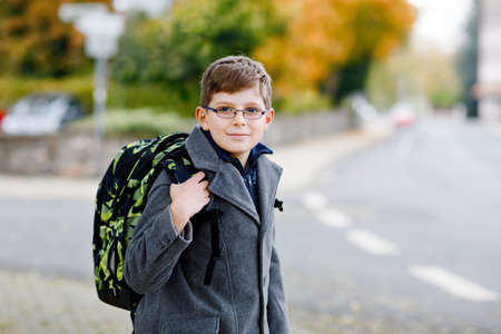 Happy kid boy with glasses and backpack or satchel. Schoolkid in stylish fashon coan on the way to middle or high school on cold autumn day. Healthy child outdoors on the street, on rainy day.の写真素材