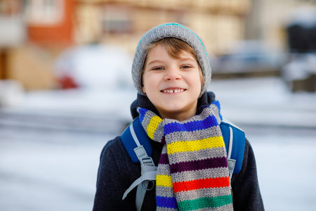 Little school kid boy of elementary class walking to school during snowfall. Happy child having fun...