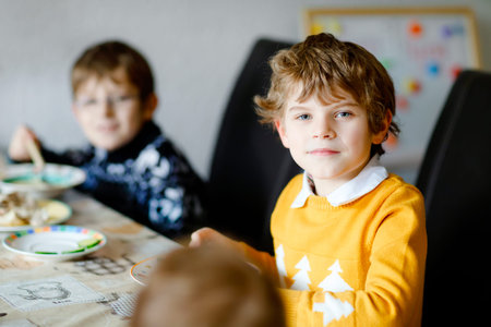 Three children, siblings eating vegetable soup at home. Two school kid boys and baby girl in...