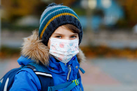 Little kid boy wearing medical mask on the way to school. Child backpack satchel. Schoolkid on cold autumn or winter day with warm clothes. Lockdown and quarantine time during corona pandemic diseaseの写真素材
