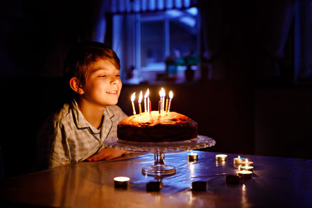 Adorable happy blond little kid boy celebrating his birthday. Child blowing candles on homemade...