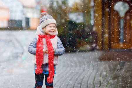 Cute little funny toddler girl in colorful winter fashion clothes having fun and playing with snow, outdoors during snowfall. Active outdoors leisure with children. Happy healthy childの写真素材