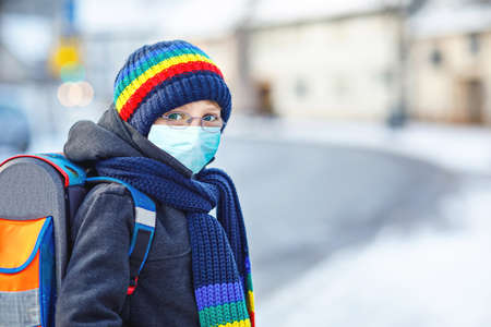 School kid boy with glasses wearing medical mask on the way to school. Child backpack satchel. Schoolkid on winter day with warm clothes. Lockdown and quarantine time during corona pandemic diseaseの写真素材