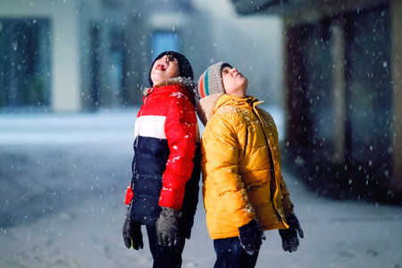 Two little kids boys of elementary class walking to school during snowfall on early dark morning....