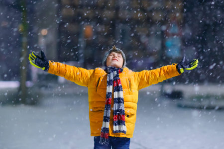 Little school kid boy of elementary class walking to school during snowfall on early dark morning....