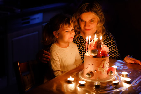 Adorable little toddler girl and mum, woman celebrating fourth birthday. Cute child daughter and happy mother blowing candles on cake. Smiling family portrait, mom love and happinessの写真素材