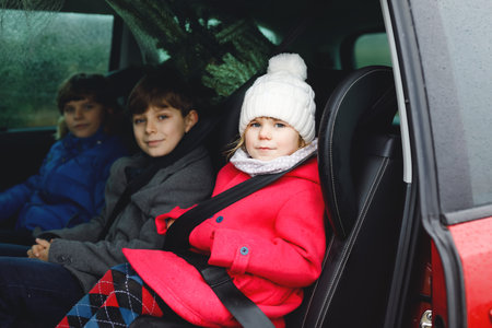 Adorable little toddler girl and two school kids boys with Christmas tree inside of family car. Happy healthy children in winter fashion clothes buying big Xmas tree for traditional celebration.の写真素材