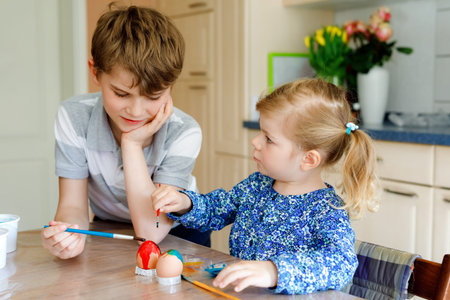 Excited little toddler girl and older brother, school kid boy coloring eggs for Easter. Two cute...