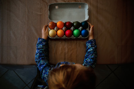Close-up of little toddler girl with colored eggs for Easter. Adorable child holding colorful egg hoarding and celebrating holiday with family.の写真素材