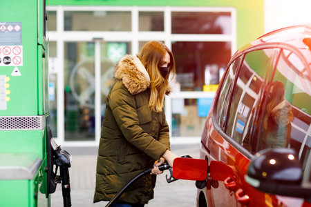 Woman wear medical mask at self-service gas station, hold fuel nozzle, refuel the car with petrol...
