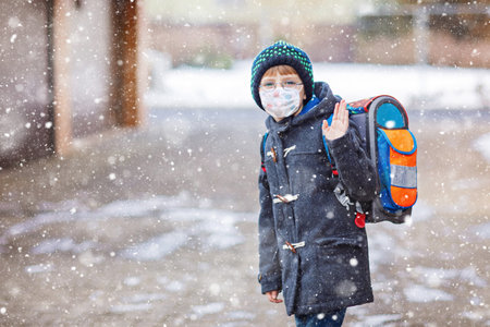 Little kid boy with glasses wearing medical mask on the way to school after lockdown. Child backpack satchel. Schoolkid on winter day with warm clothes.の写真素材