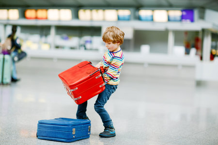 Happy little kid boy with big suitcase luggage at terminal on international airport. Preschool excited child wait for flight and going on vacations. Travel family lifestyle.の写真素材
