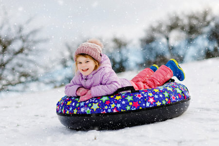 Active toddler girl sliding down the hill on snow tube. Cute little happy child having fun outdoors in winter on sledge . Healthy excited kid tubing snowy downhill, family winter time.の写真素材