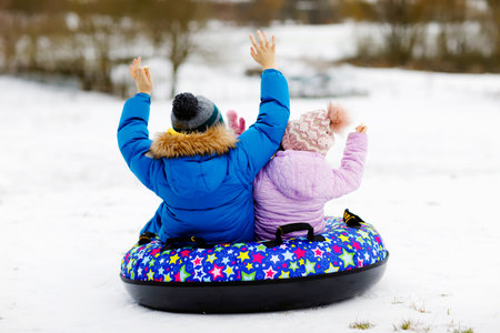 Active toddler girl and school boy sliding together down the hill on snow tube. Children, siblings having fun outdoors in winter on sledge. Brother and sister tubing. No face, unrecognizable personの写真素材