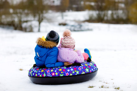 Active toddler girl and school boy sliding together down the hill on snow tube. Children, siblings having fun outdoors in winter on sledge. Brother and sister tubing. No face, unrecognizable personの写真素材