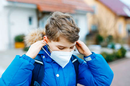Kid boy wearing ffp medical mask on the way to school. Child backpack satchel. Schoolkid on cold autumn or winter day with warm clothes.の写真素材