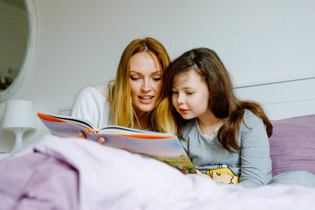 Loving mother and school kid girl reading book together. Happy family, woman and cute daughter...